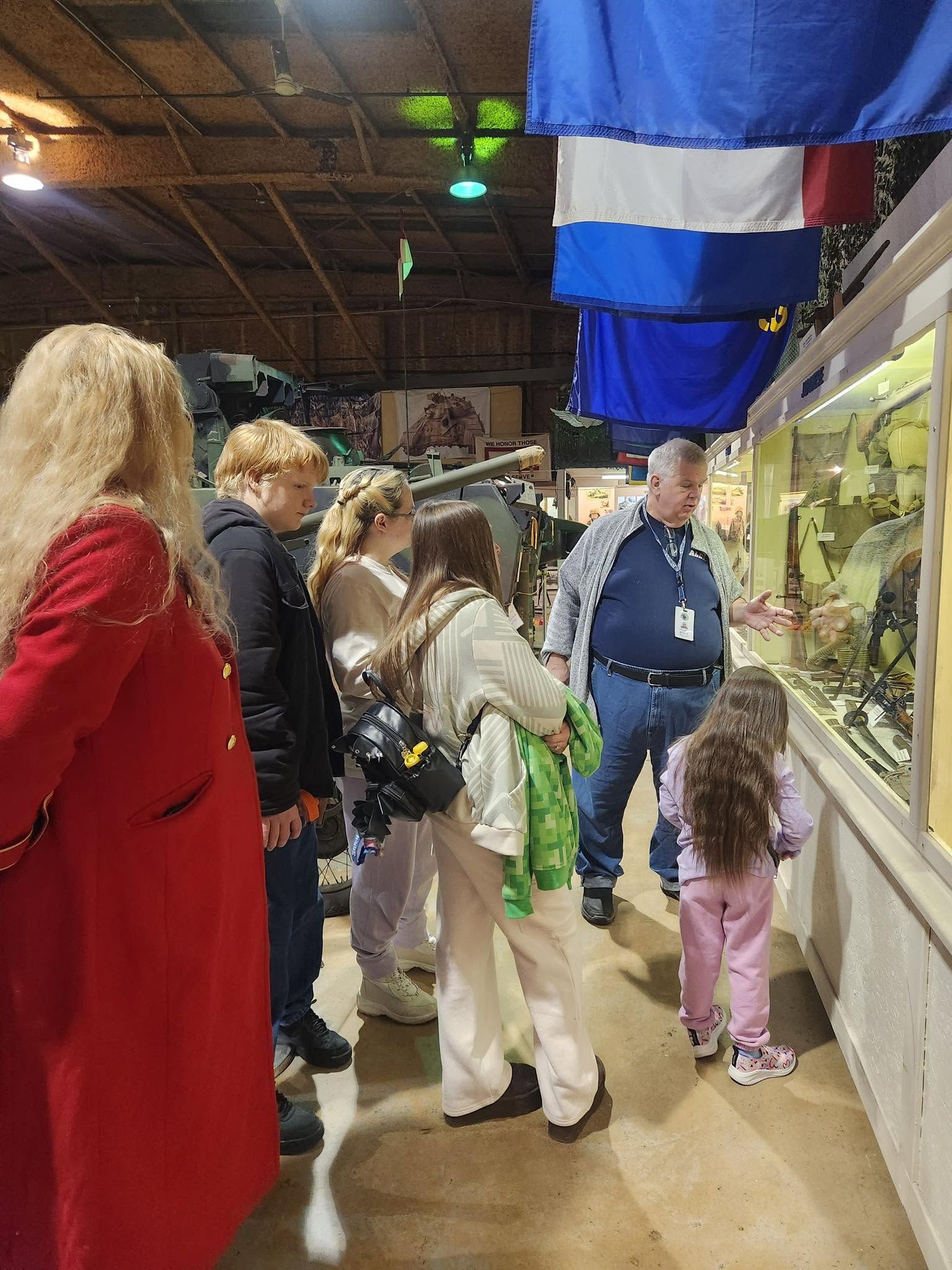 People standing in a museum or exhibit hall beside glass displays and hanging flags.
