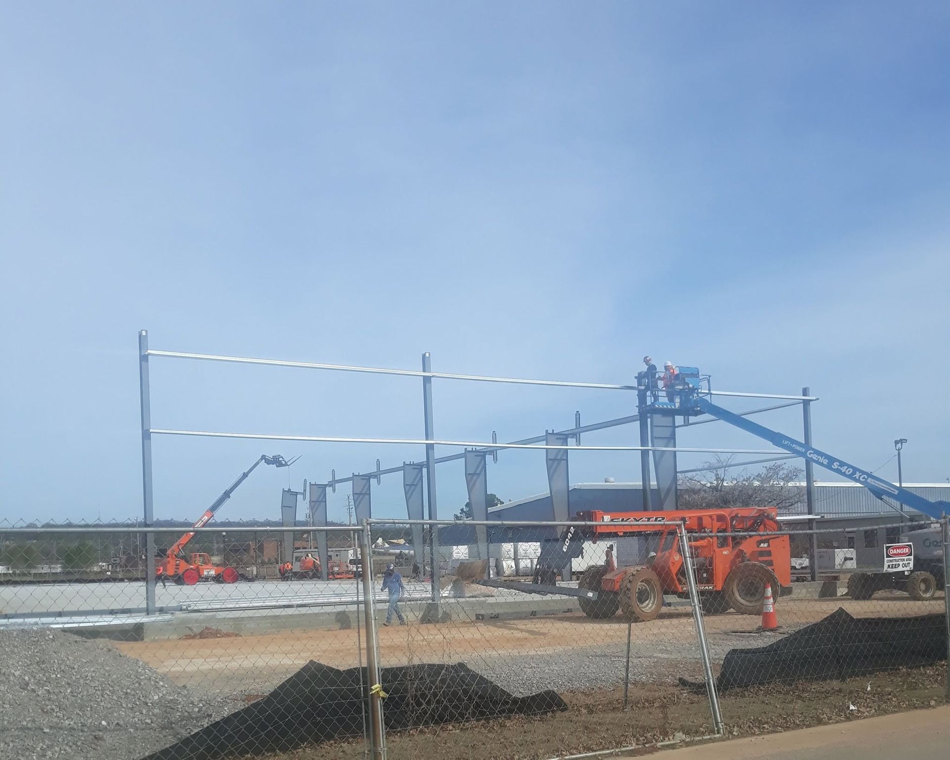 Construction site with orange heavy equipment, steel frames, and a blue crane under a clear sky