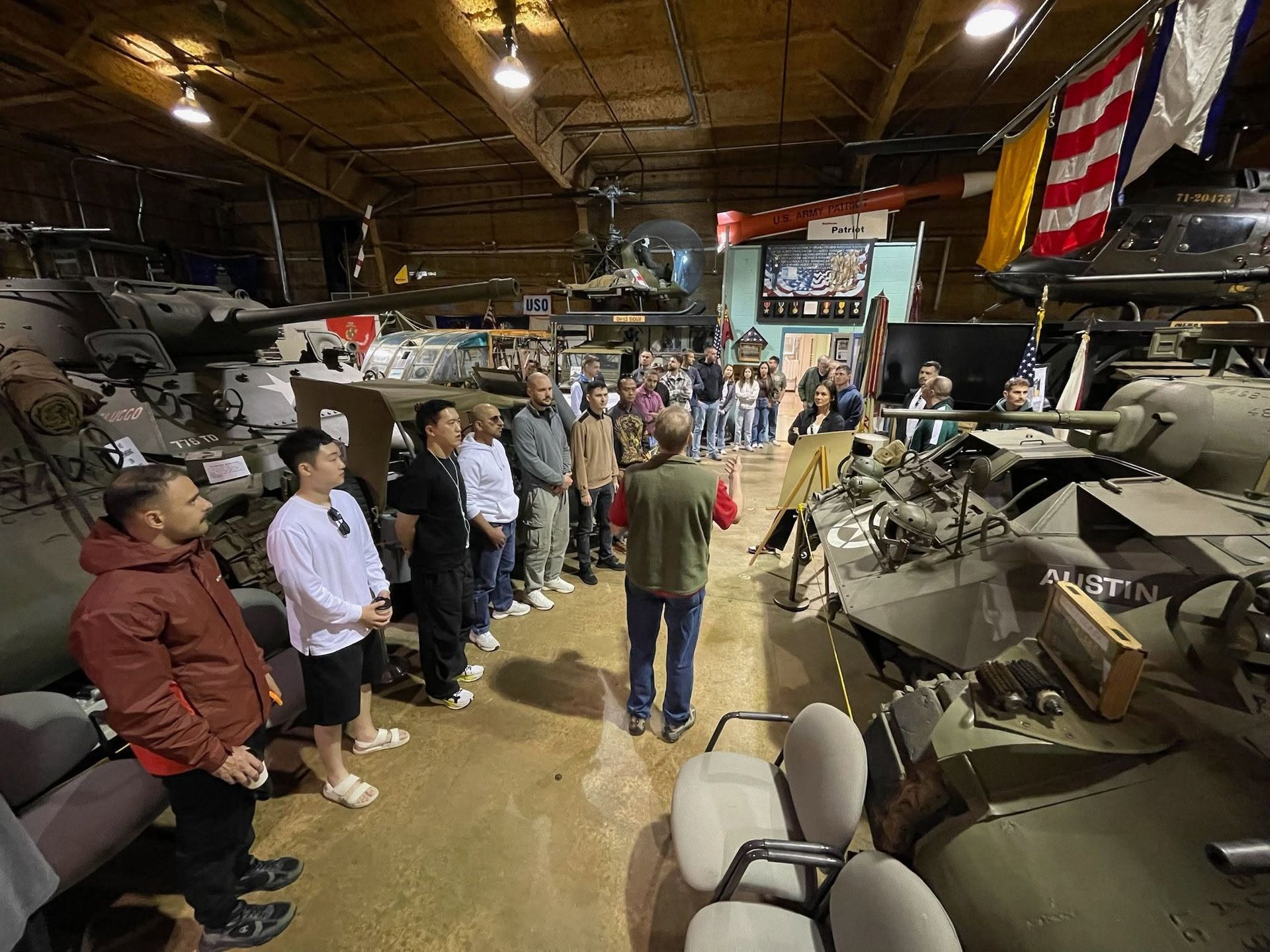 Visitors stand among military vehicles and tanks inside a large museum hall.