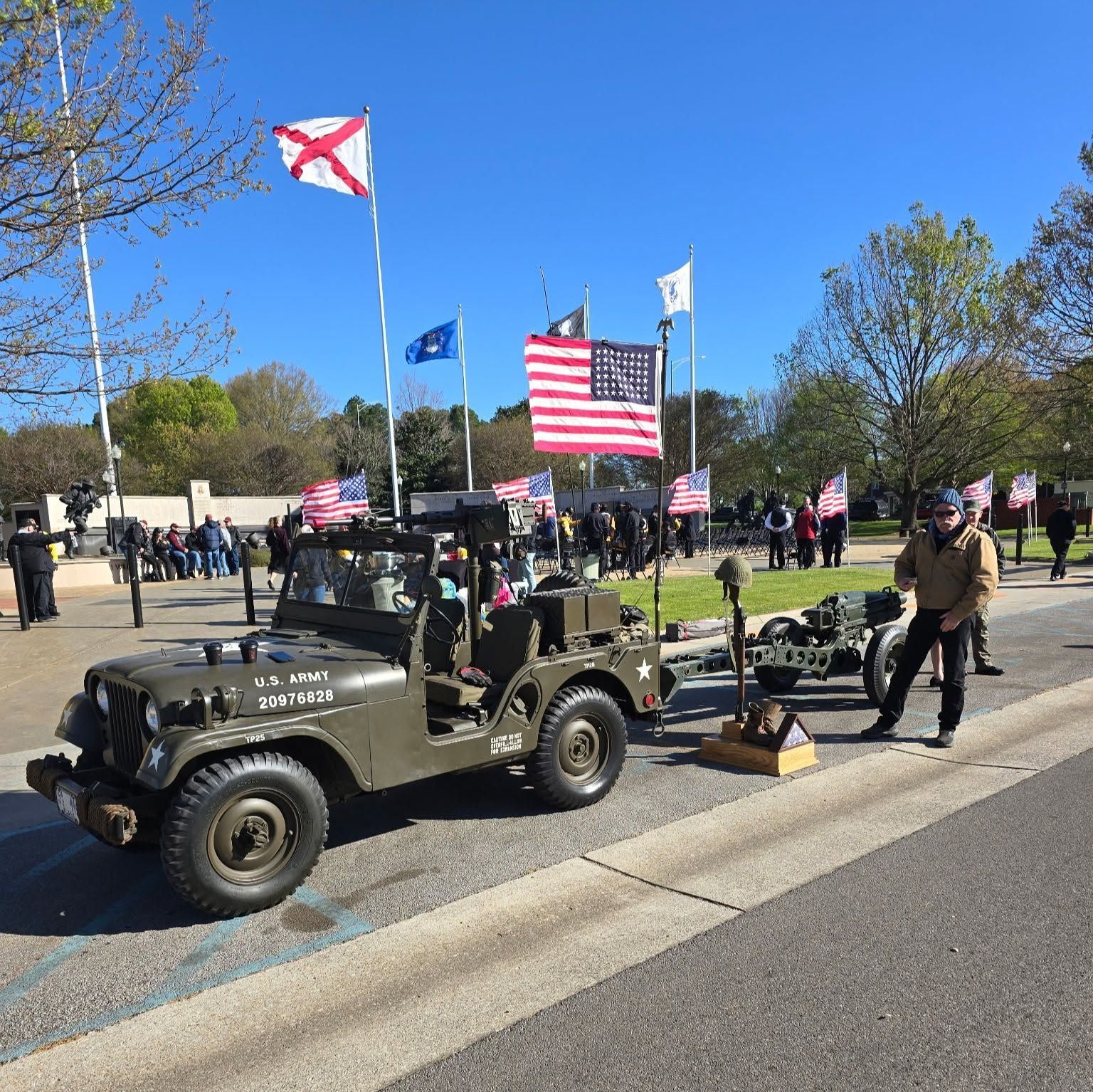 Veterans gathering with military jeep and U.S. flags in a park on a sunny day