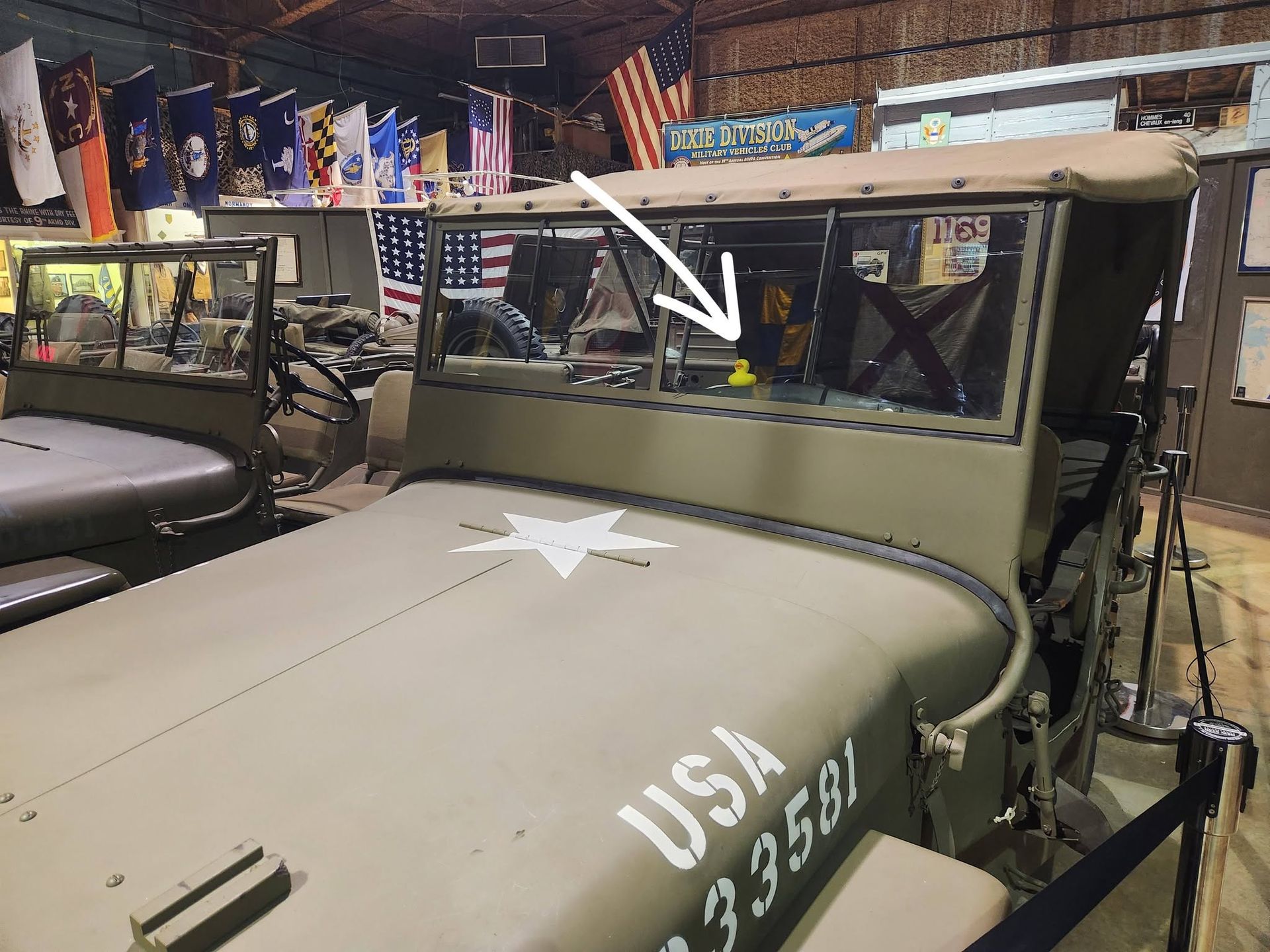 Old military jeep in a workshop, olive drab with white stenciling and a white arrow on the hood.