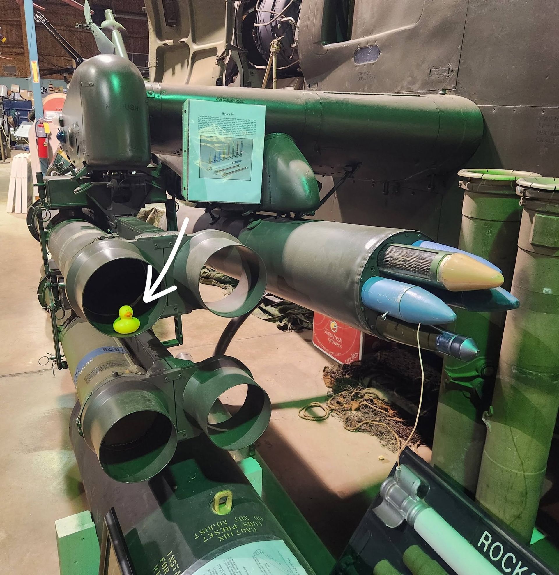 Green metal sci-fi prop with blue cones and pipes in a workshop; white arrow points to a small yellow part.