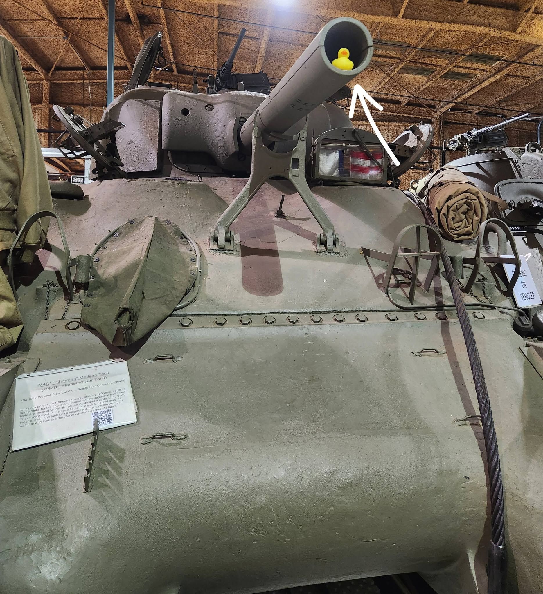 Green tank with a mounted cannon inside a museum exhibit, surrounded by ropes and display items