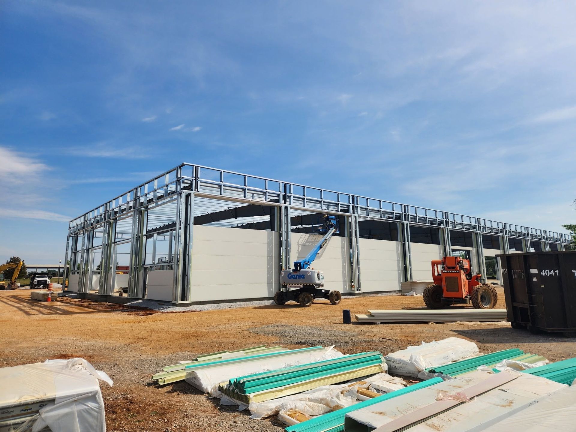 Partially built steel-framed construction site with materials and machinery under a blue sky