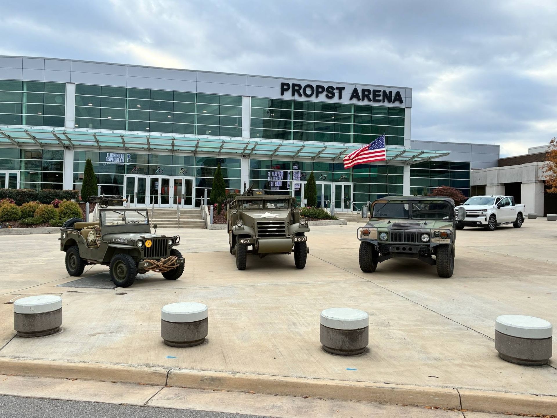 Military vehicles parked outside Propst Arena with a U.S. flag flying in front of the building