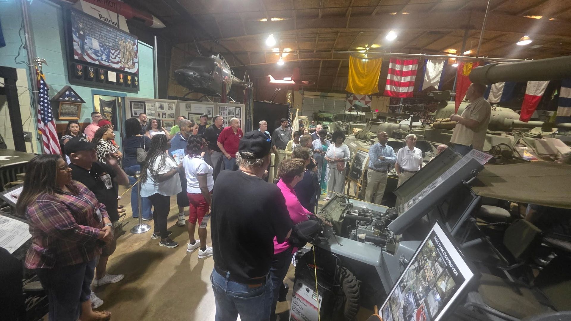 Crowded indoor market aisle with people gathered around stalls and merchandise under hanging signs