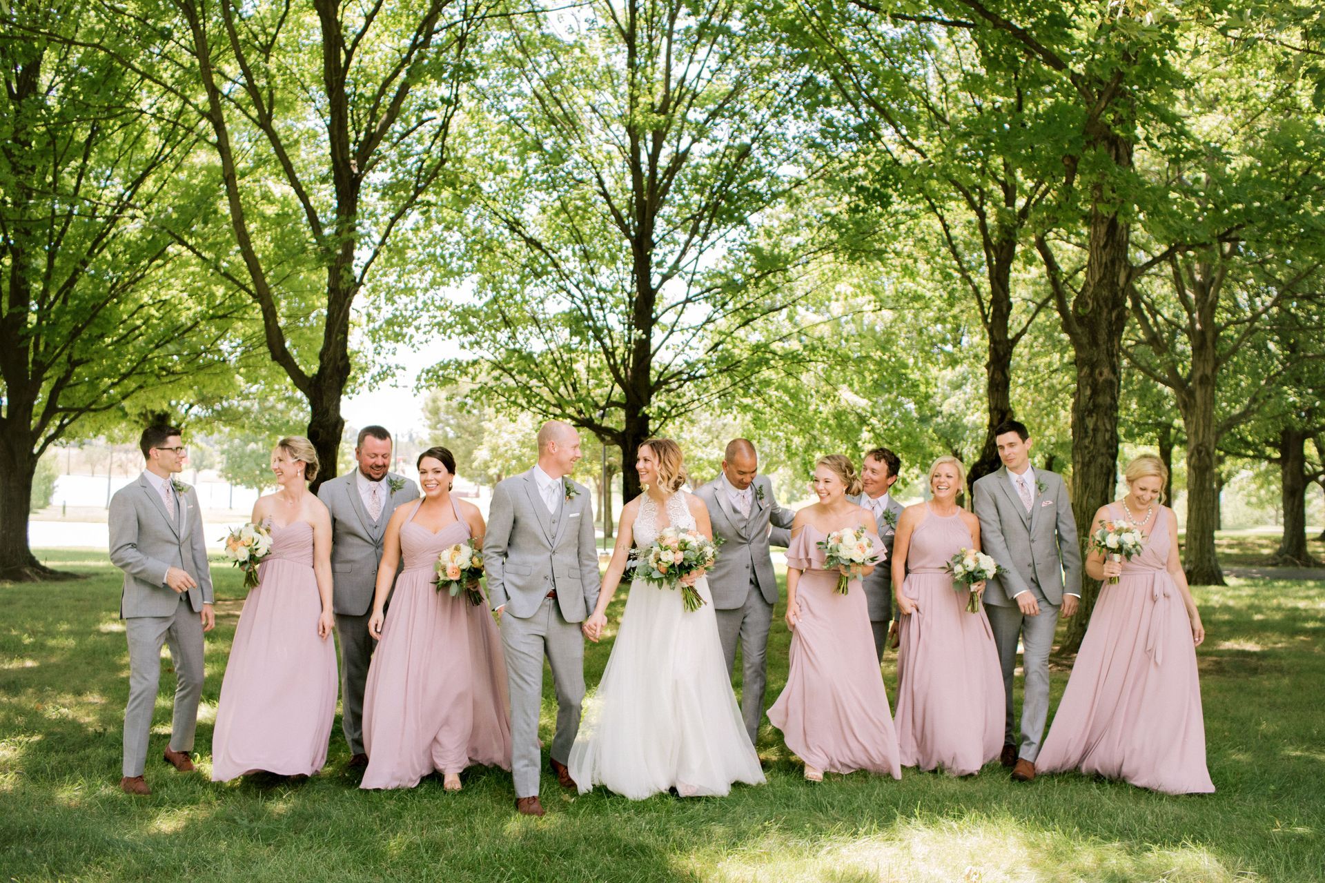 A bride and groom are posing for a picture with their wedding party in a park.
