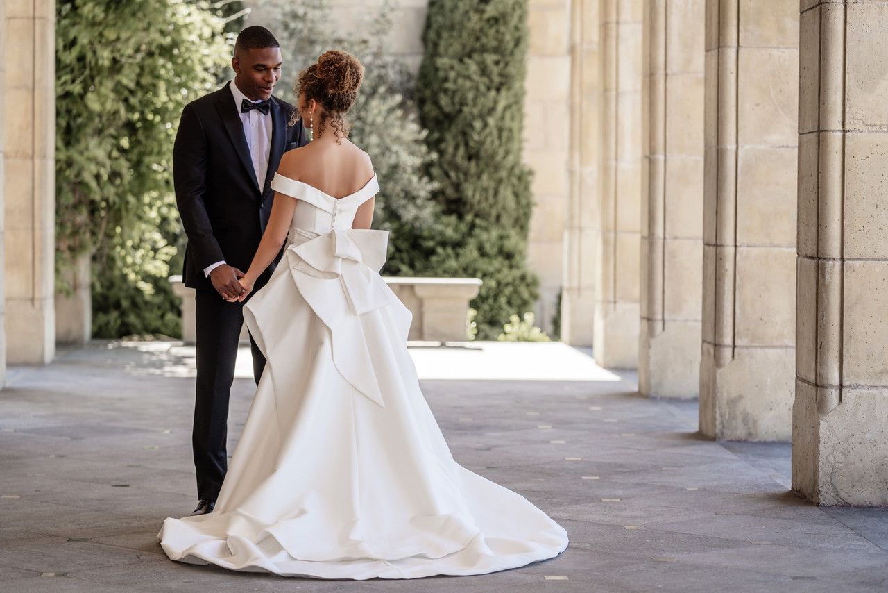 A bride and groom are standing next to each other holding hands.