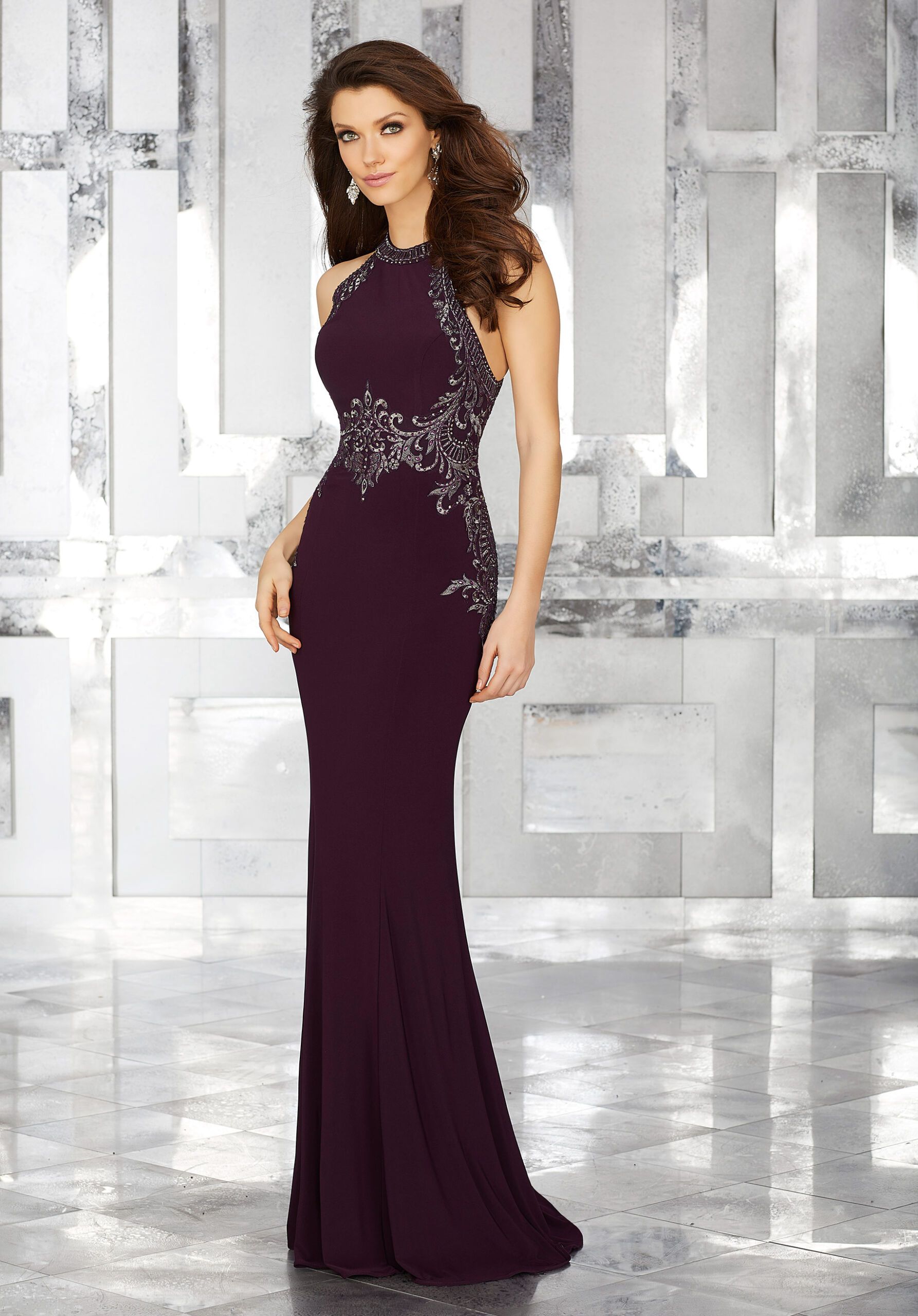 A woman in a purple dress is standing in front of a white wall.