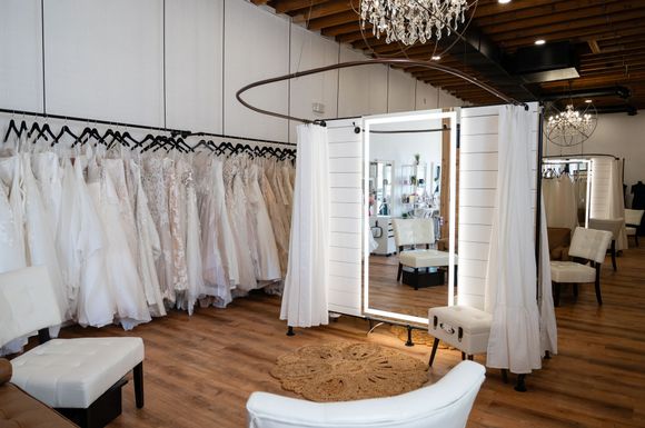 A room filled with lots of white dresses and a large mirror.