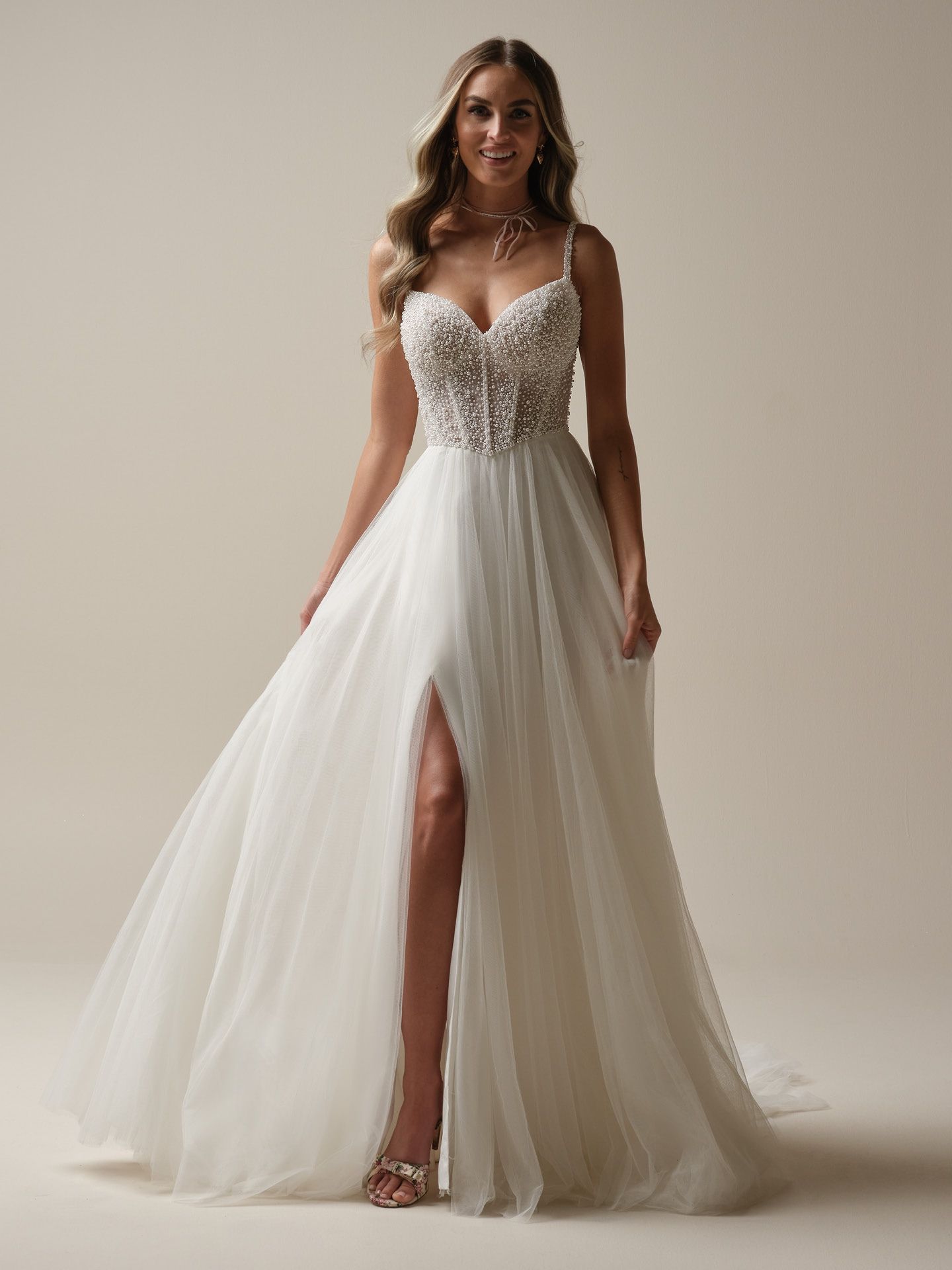 Woman in a white wedding dress with a slit, embellished bodice, and thin straps. She is smiling.