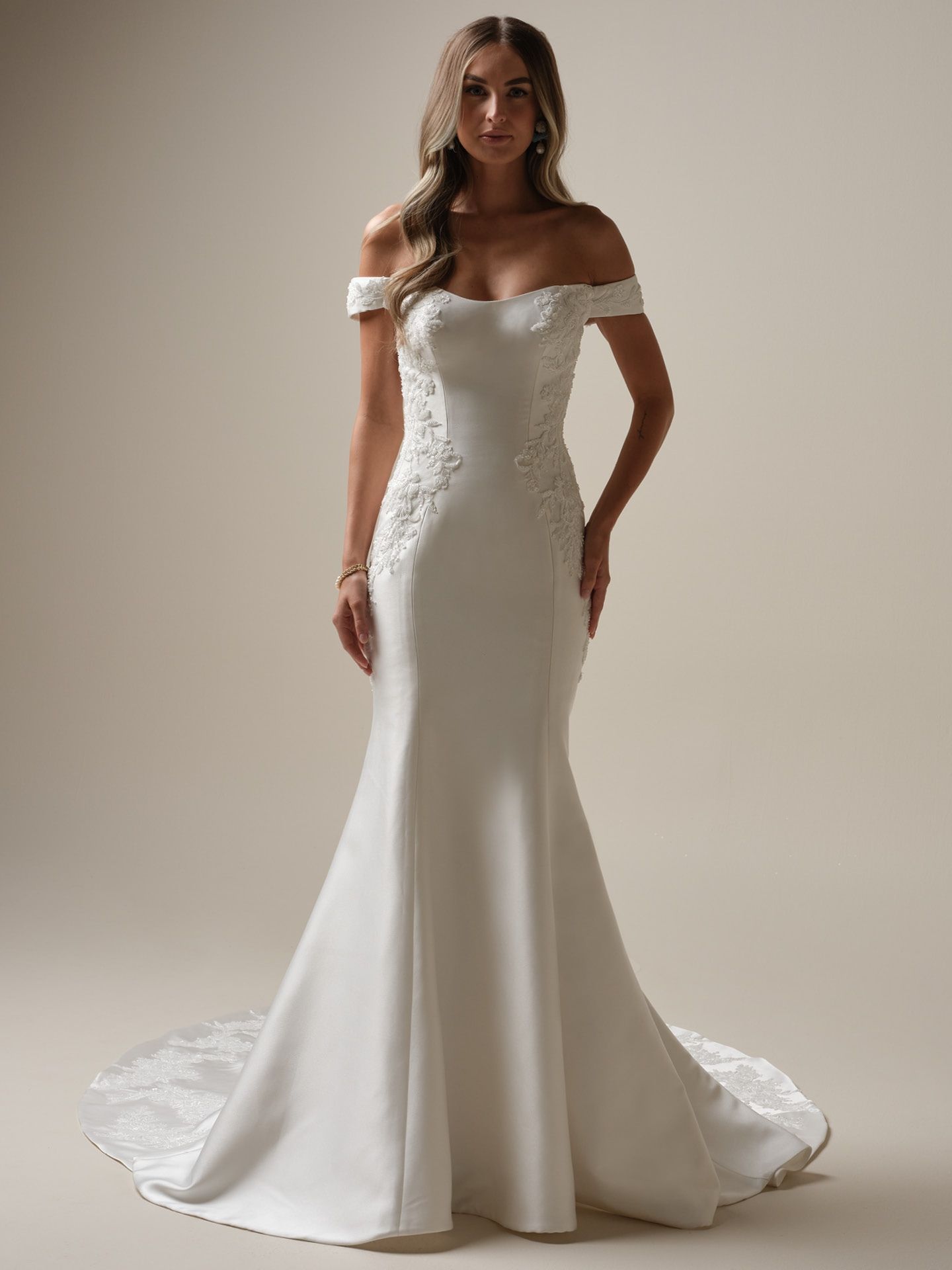 Woman in off-the-shoulder white wedding gown with train, posed in a studio.