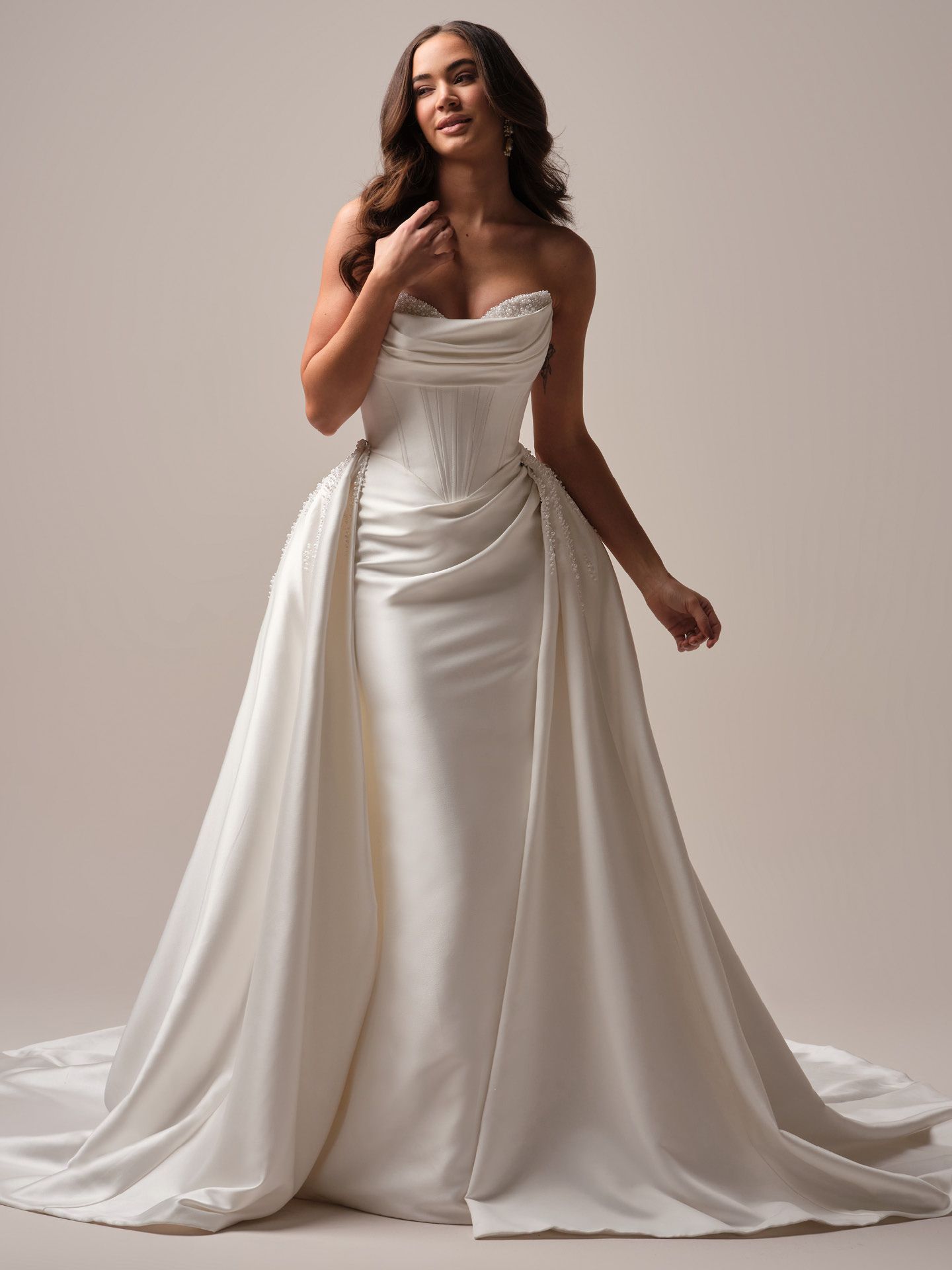 Woman in a white strapless wedding dress with train, standing in a studio, looking up and smiling.