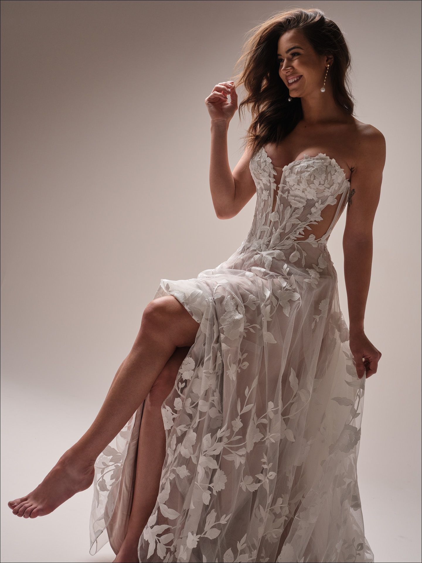 Woman in strapless white lace wedding dress, seated, smiling.