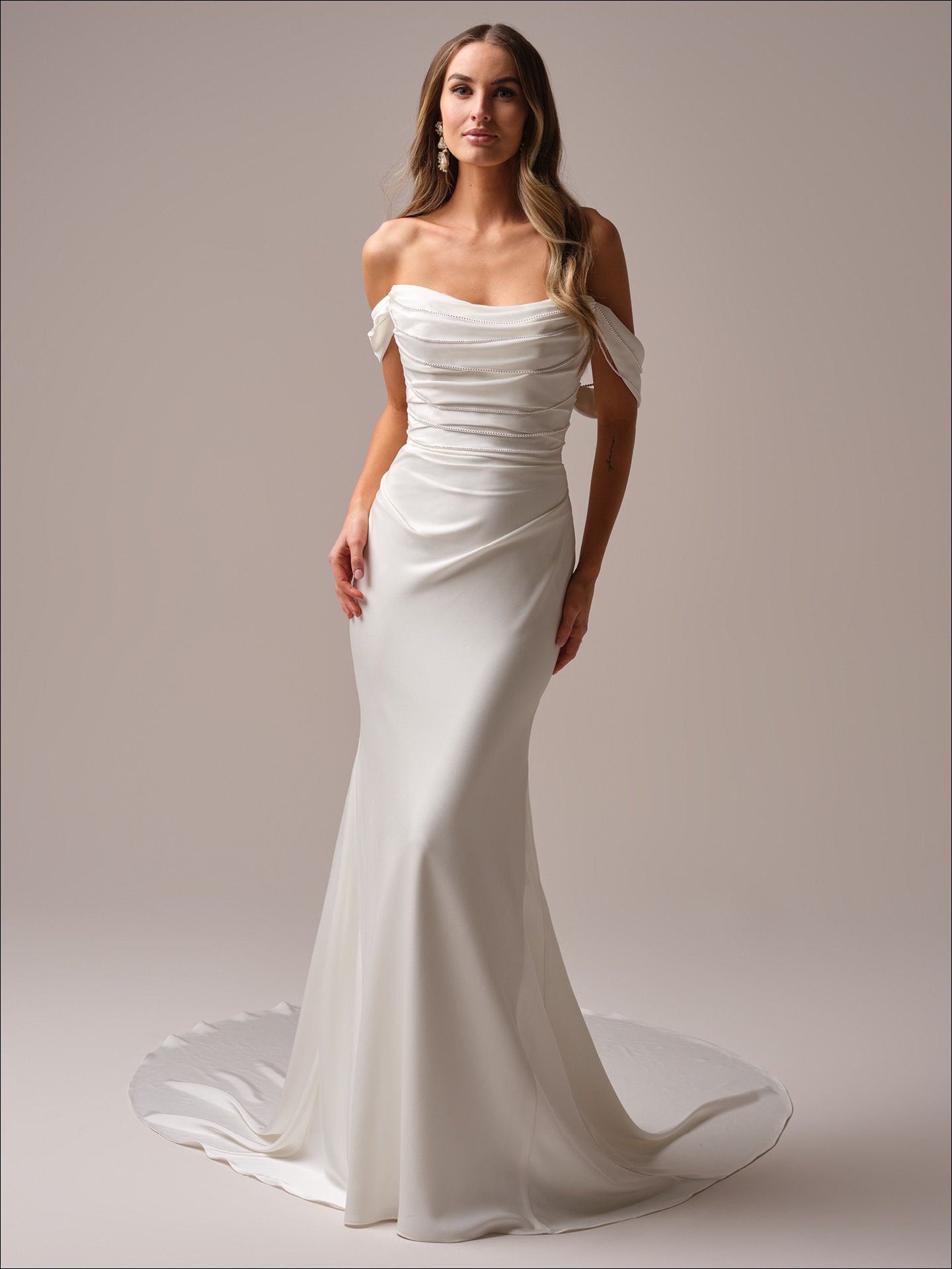 Woman in an off-the-shoulder white wedding dress, posing in a studio.