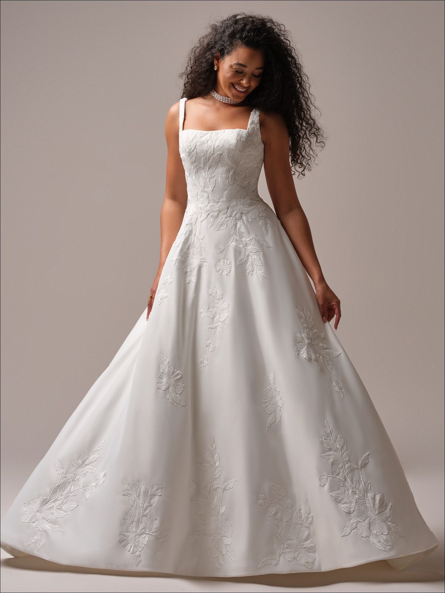 Woman wearing a white wedding dress with lace details and a square neckline, smiling.