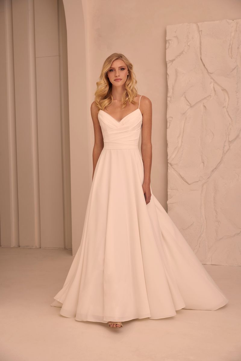 A woman in a white wedding dress is standing in front of a wall.