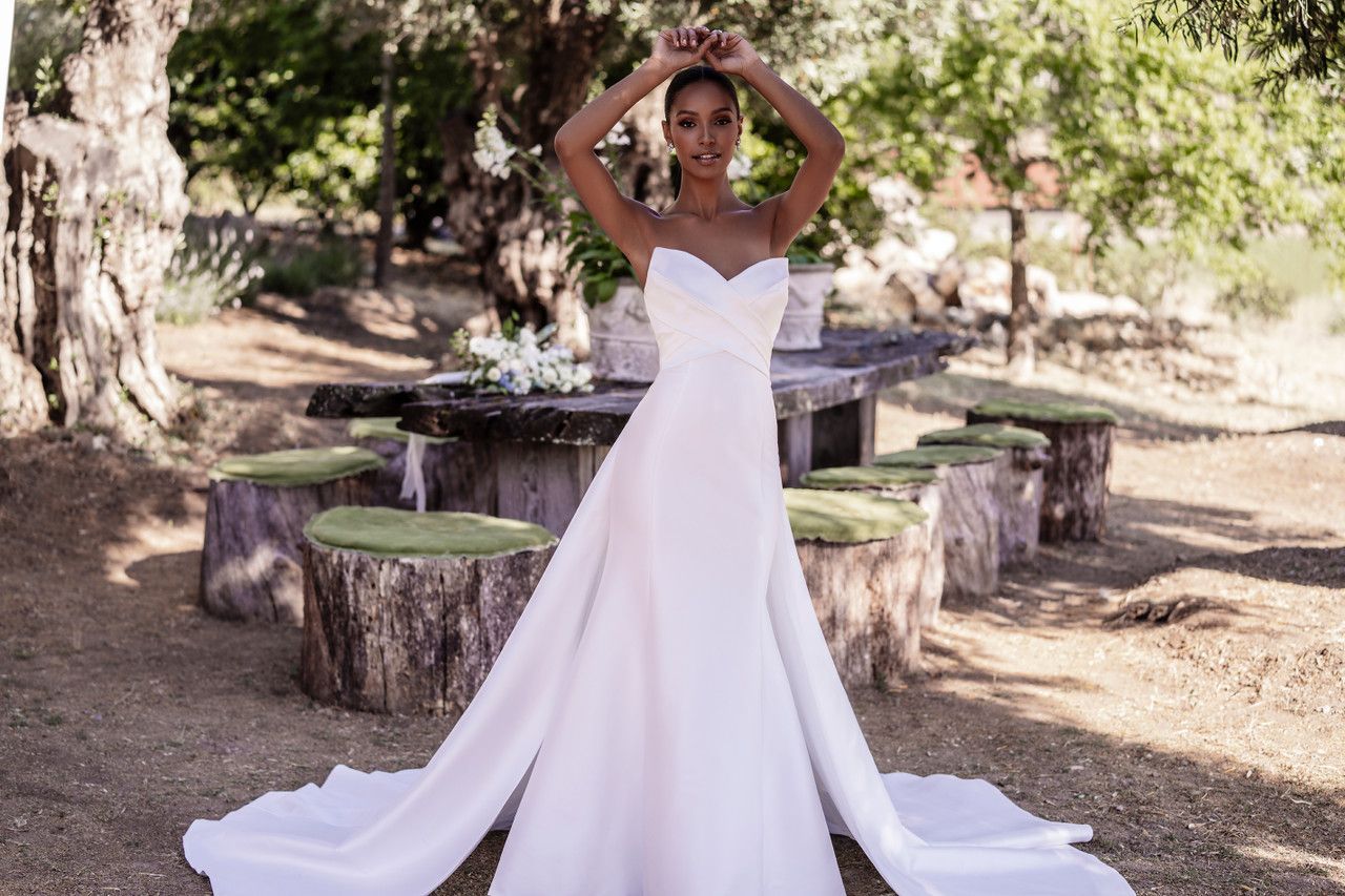 A woman in a white wedding dress is standing in front of a wooden table.