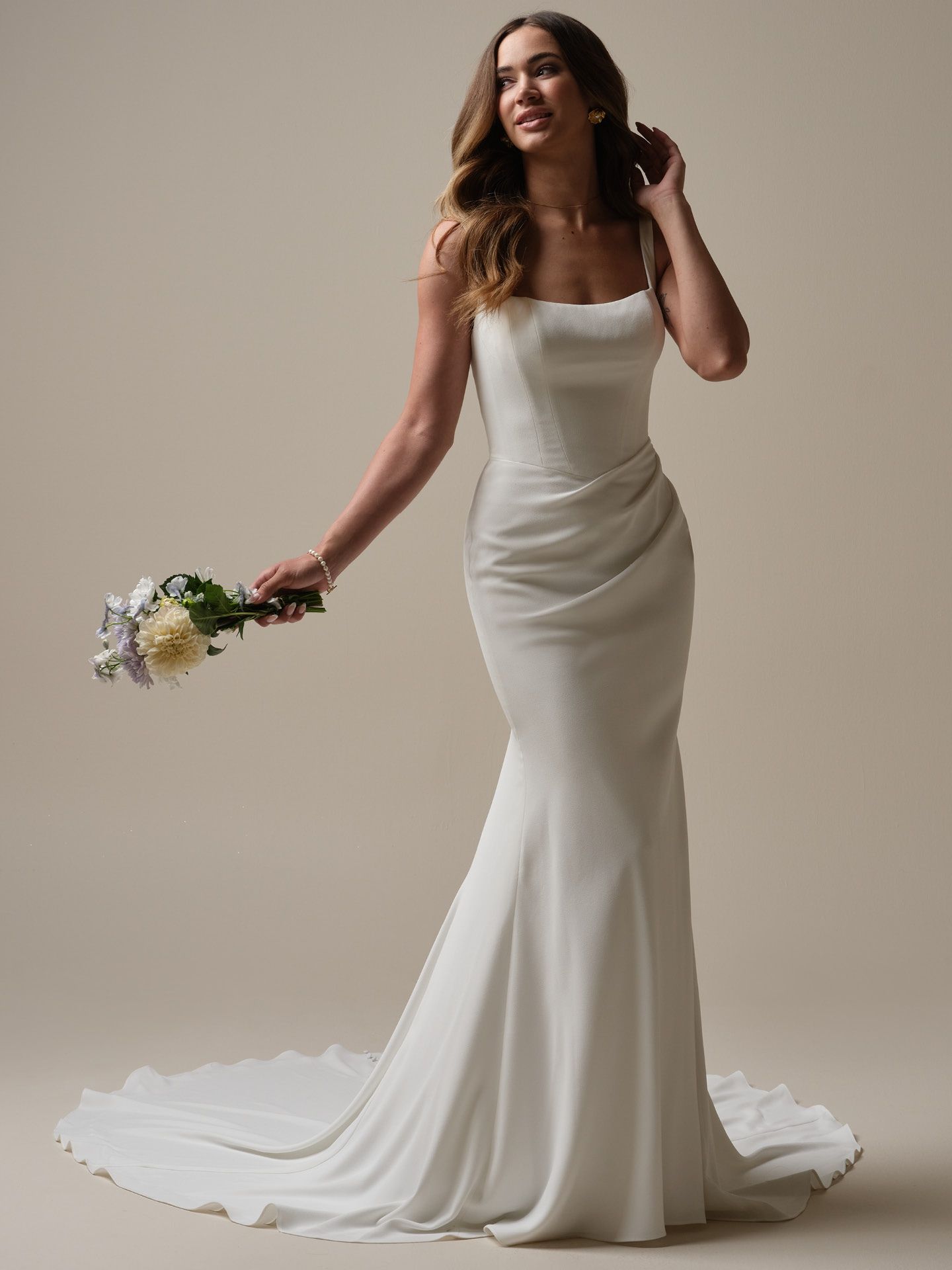 Woman in a white wedding dress holds flowers, looking up.
