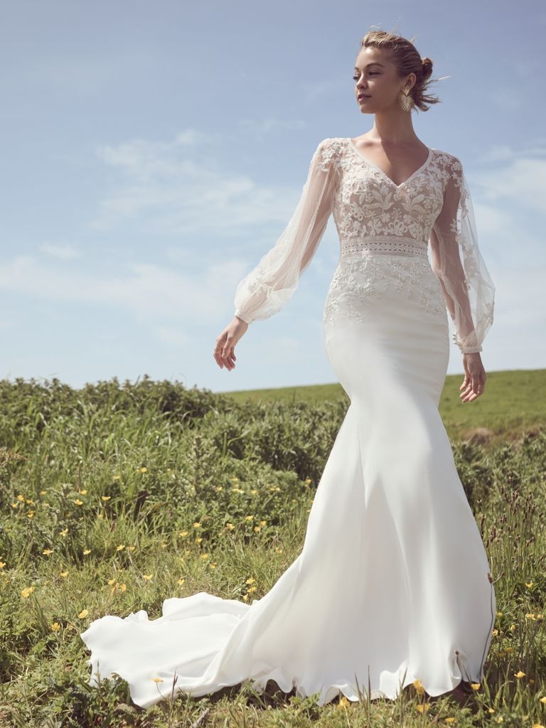 A woman in a white wedding dress is standing in a field.