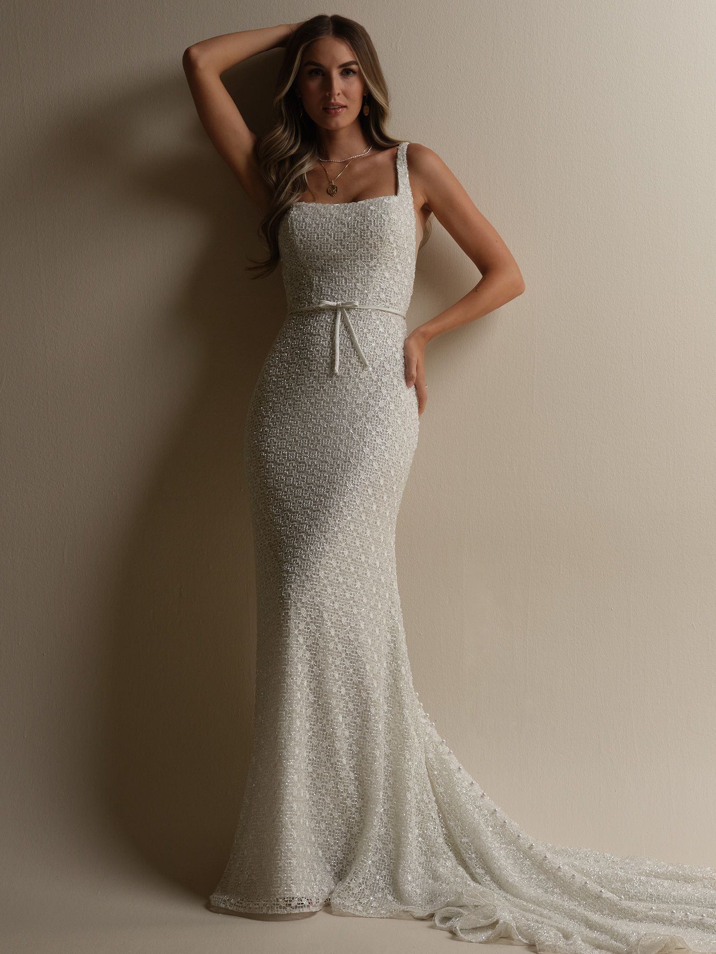 Woman in a sparkling white wedding dress, posing against a light background.