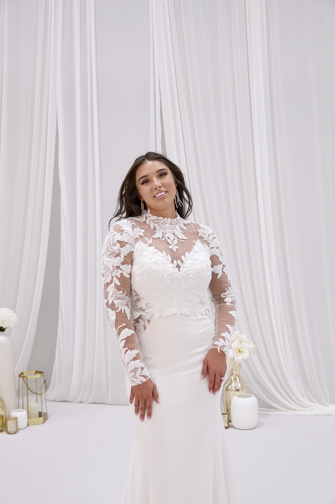 A woman in a white wedding dress is standing in front of a white curtain.