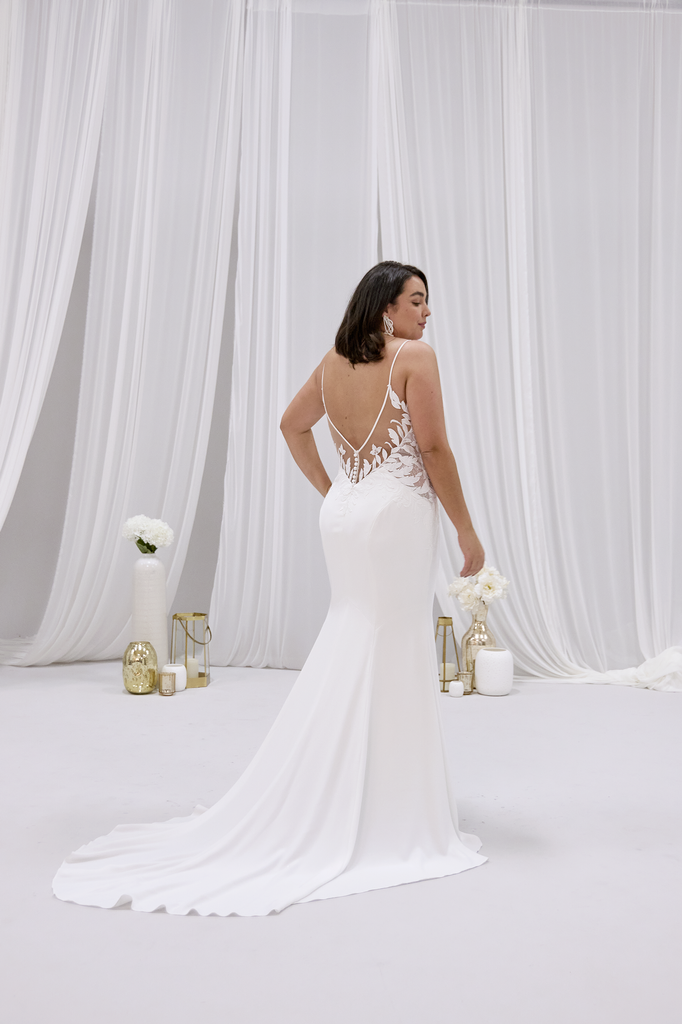 A woman in a white wedding dress is standing in front of a white curtain.