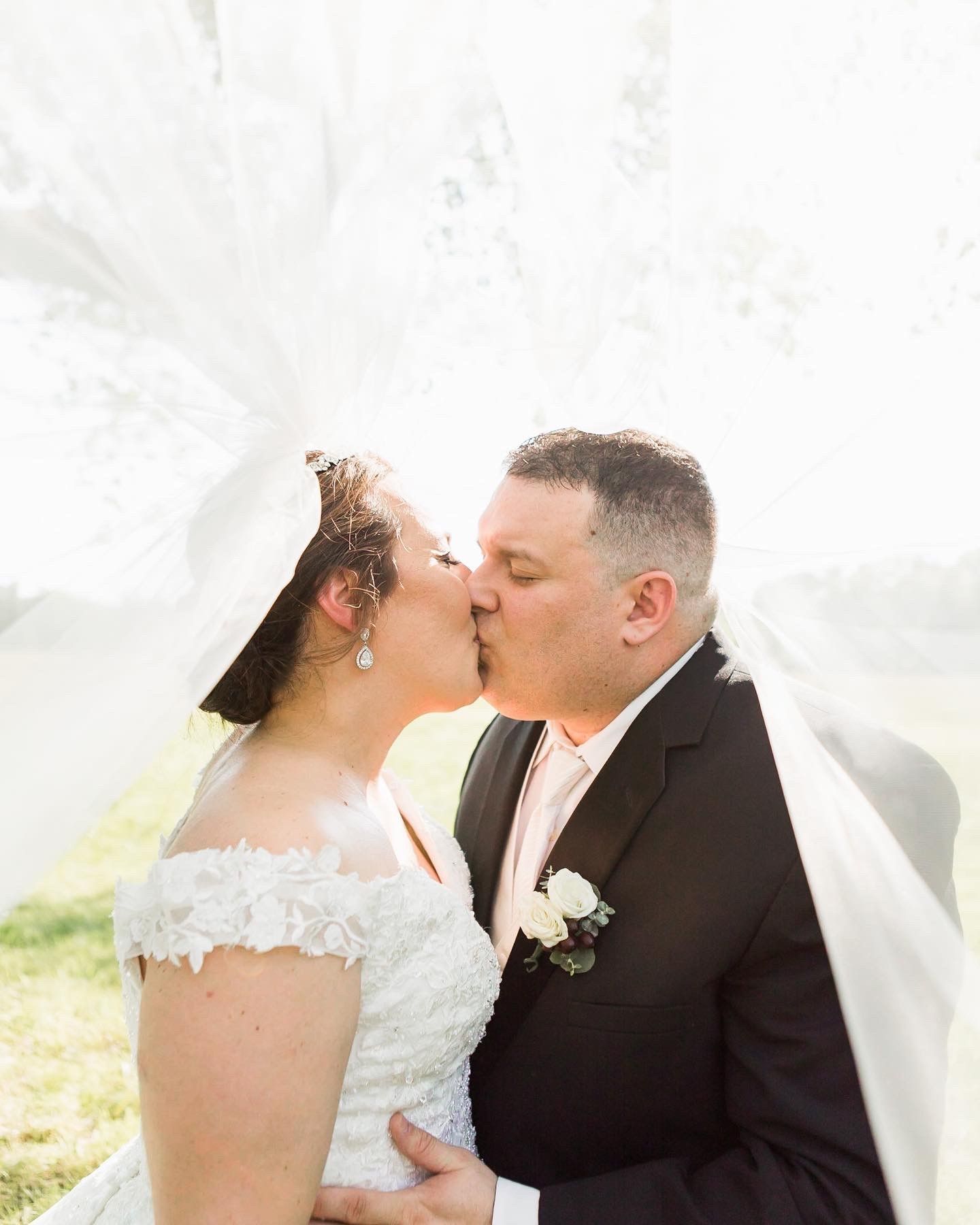 A bride and groom are kissing under a veil.