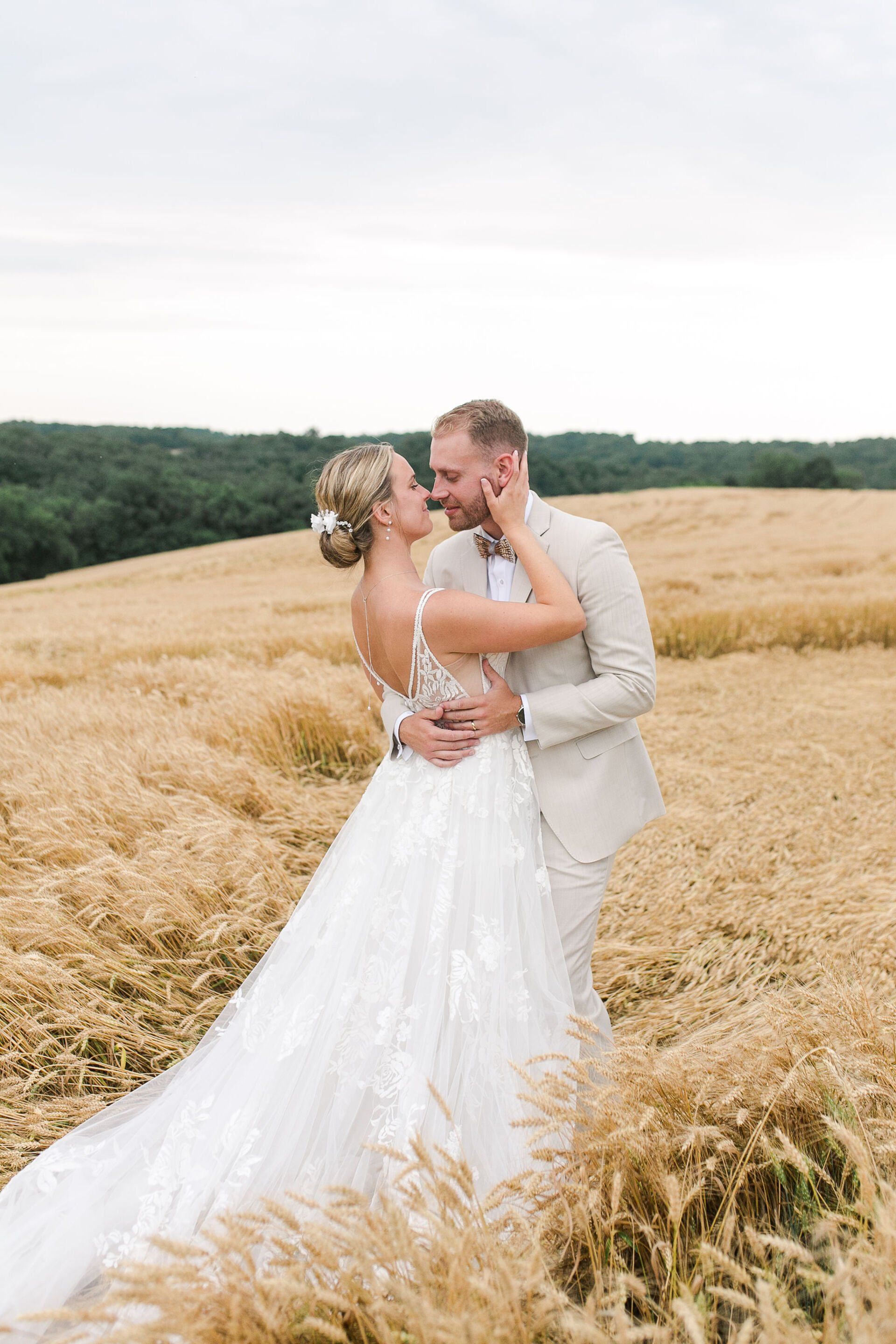 A bride and groom are kissing in a field of wheat.