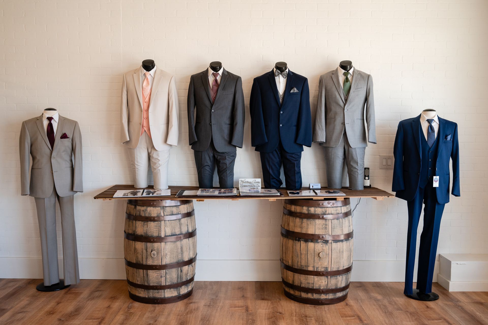 A row of men 's suits are displayed on barrels in a room.