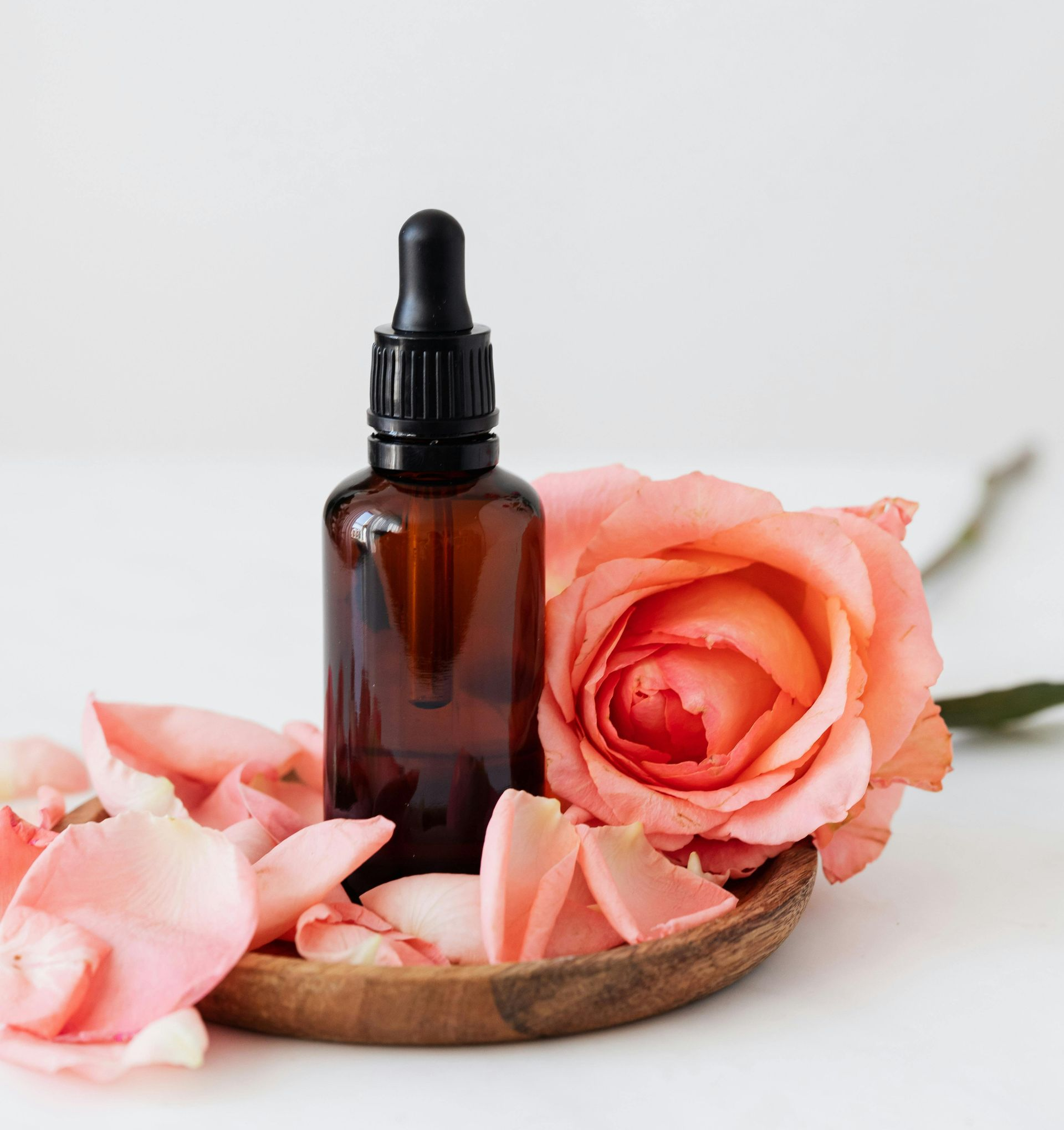 Brown essential oil bottle with dropper and pink rose petals.