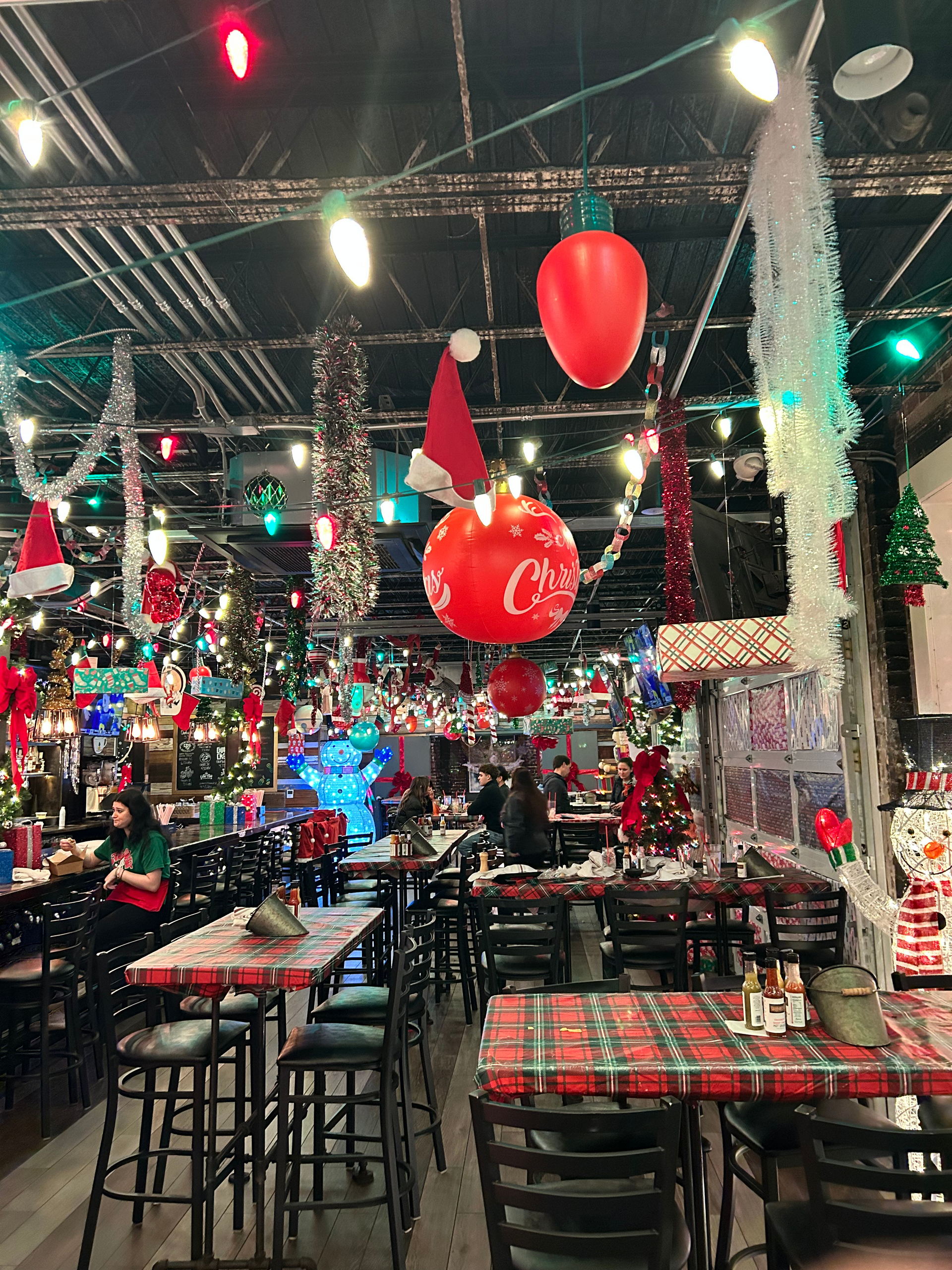 Restaurant interior decorated with Christmas lights, ornaments, and red plaid tablecloths.