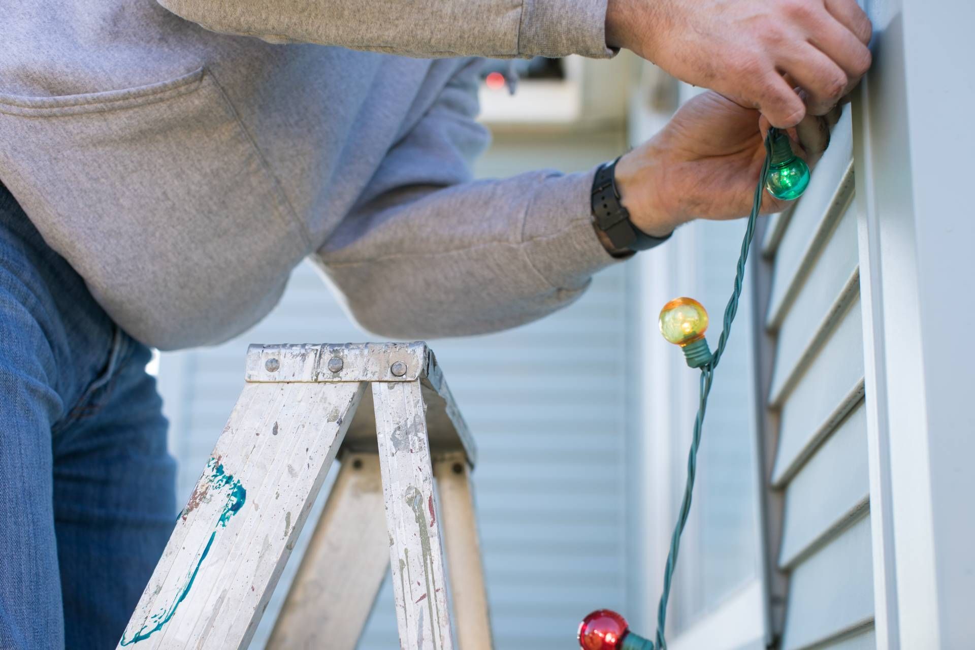 Professional installing Christmas lights along a house