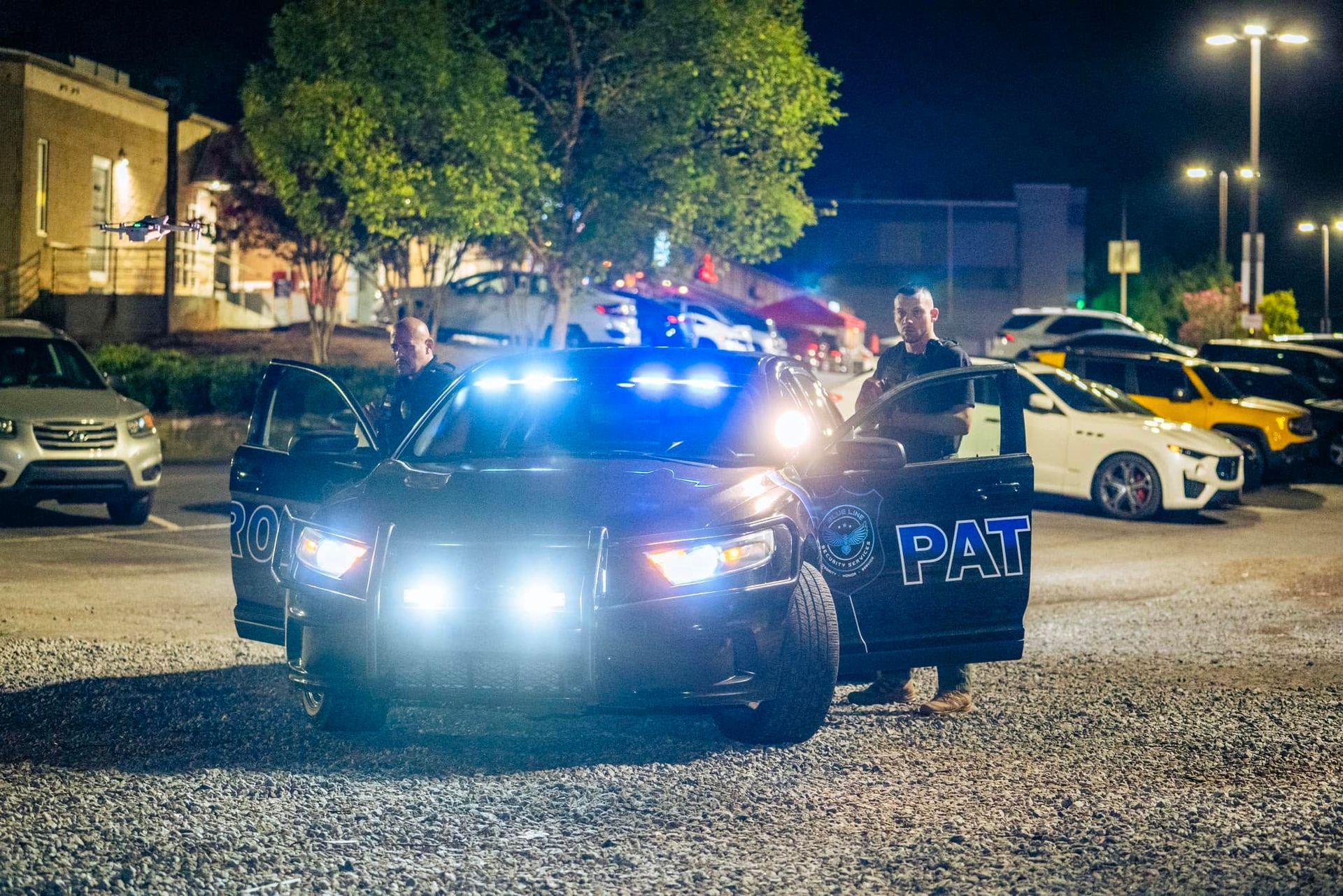 Police SUV with flashing lights parked at night in a lit lot, surrounded by other vehicles.