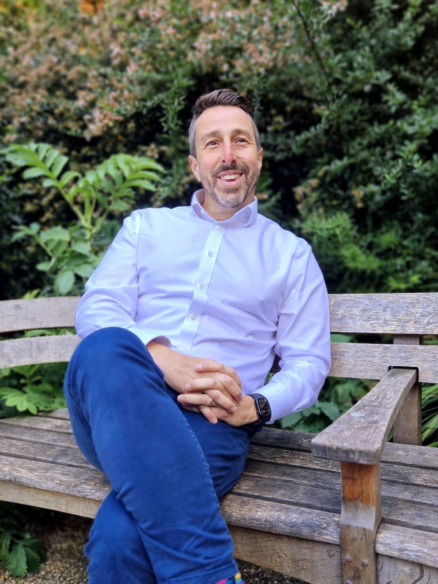 A man is sitting on a wooden bench with his legs crossed.