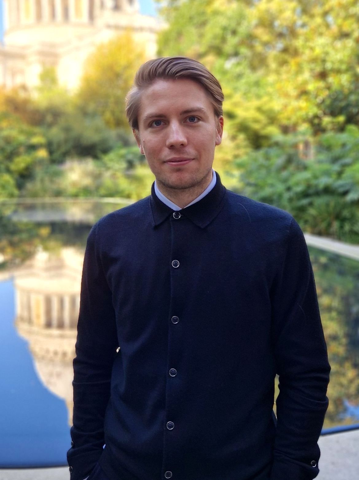 A man in a black shirt is standing in front of a fountain.