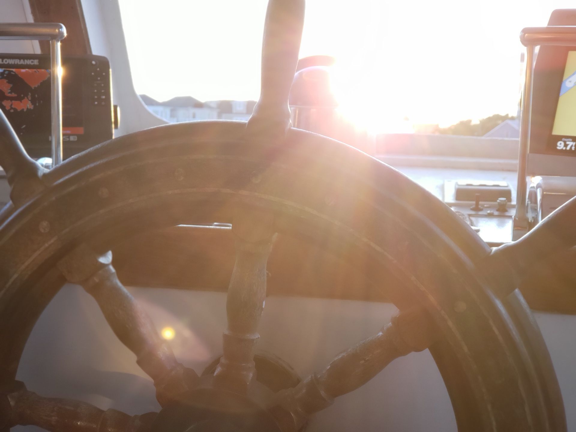Steering wheel of a boat with bright sunlight in the background.