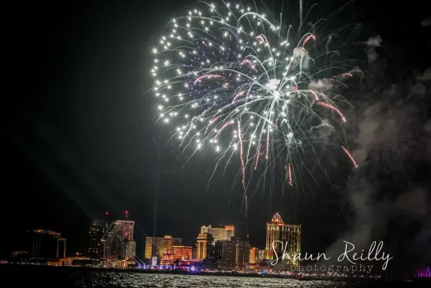 Fireworks exploding over a city skyline at night above a waterfront.