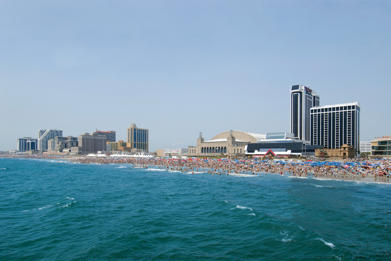 Beach with many people, Atlantic City skyline in background; blue water and sky.