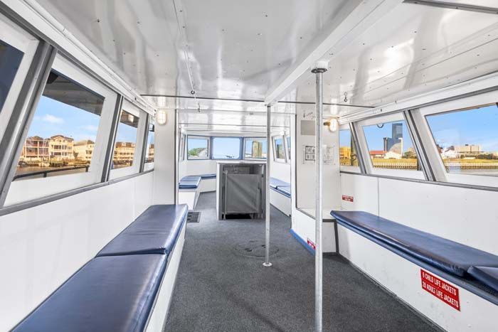 Interior of a boat with blue bench seating along the white walls and large windows, gray carpet.