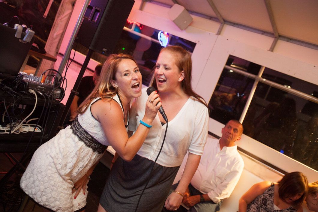 Two women singing karaoke, one with a microphone, in a brightly lit room.