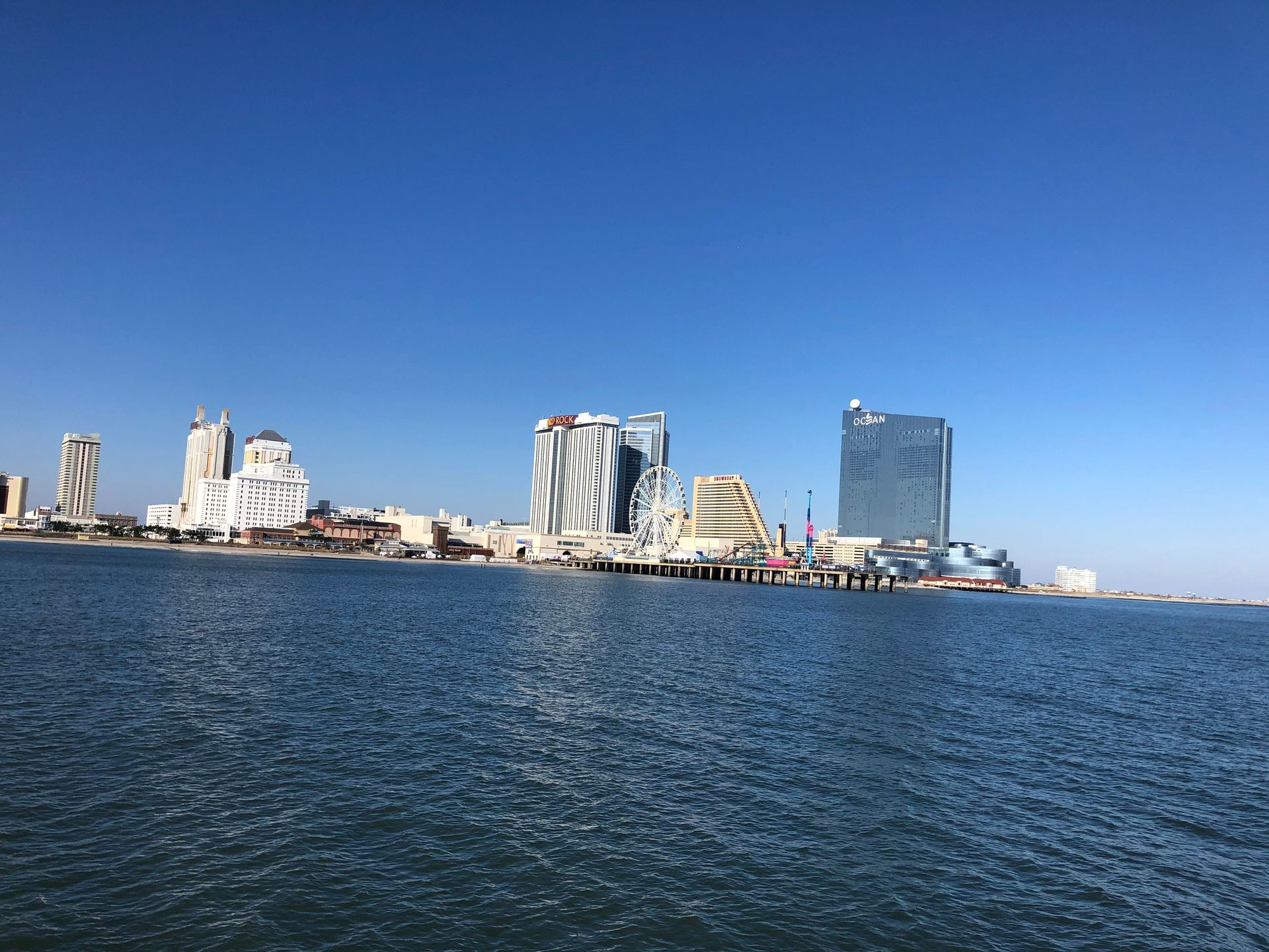 City skyline with various modern buildings along a coastline under a clear blue sky.