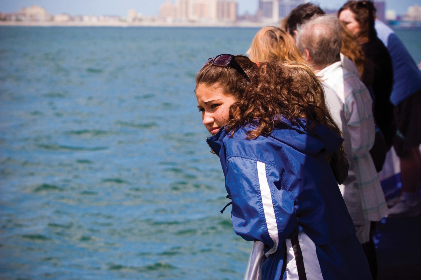 People looking out over water; the young woman in blue jacket is in focus.