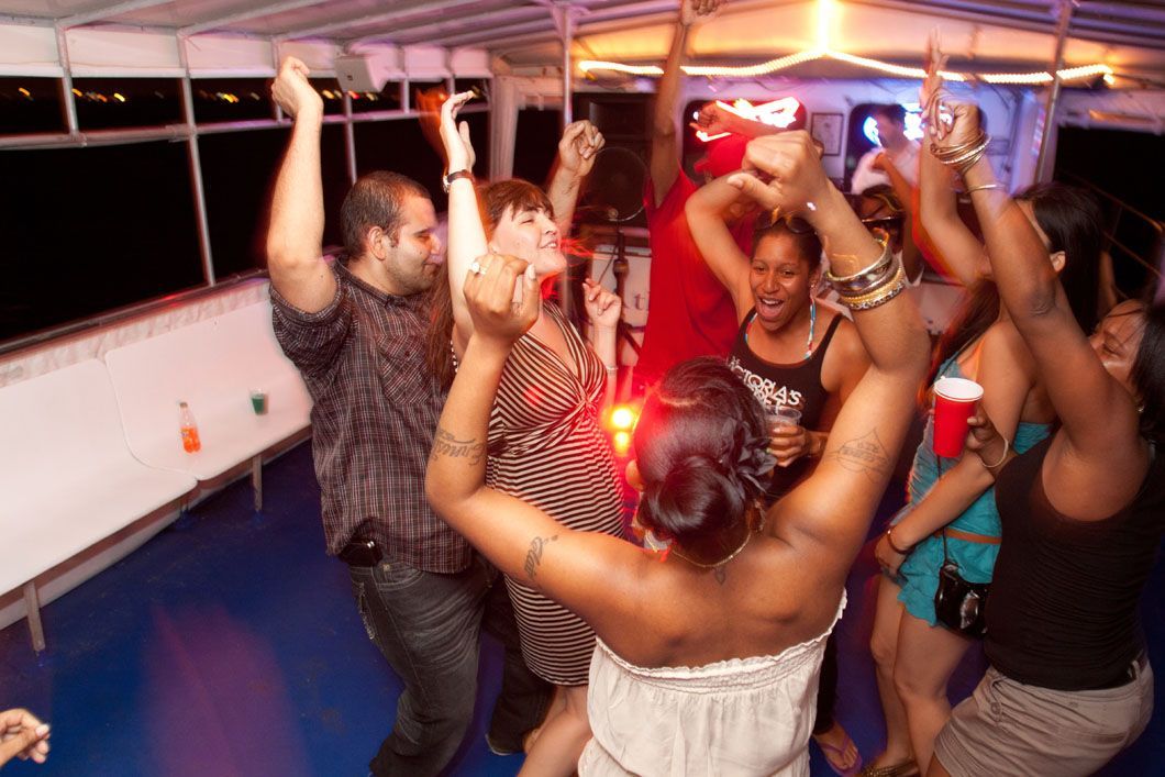 People dancing on a boat deck at night, arms raised, surrounded by party lights.