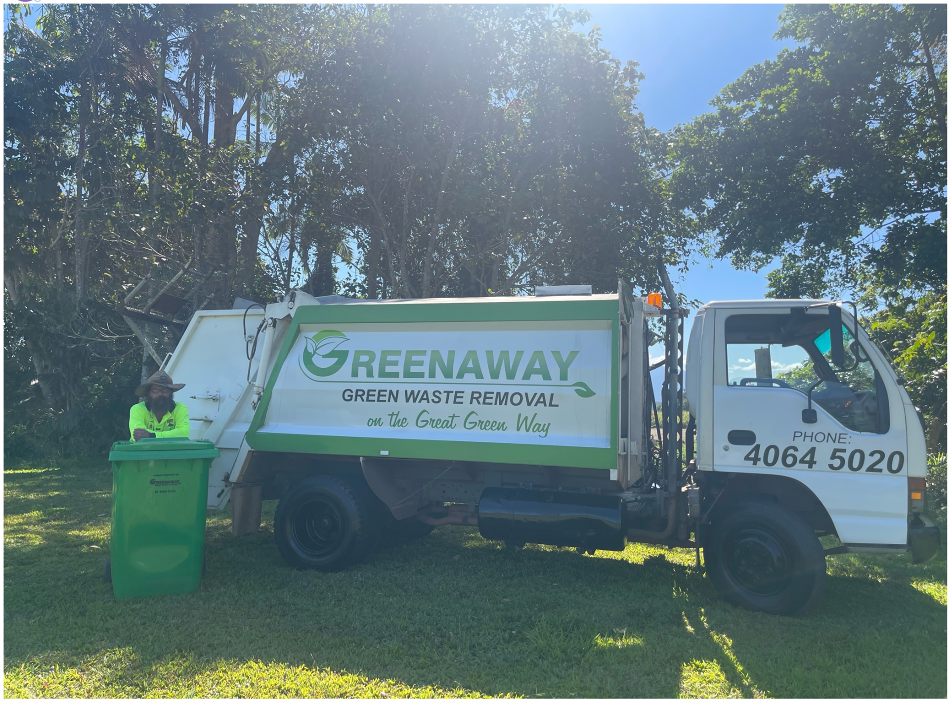 Greenaway garbage truck with green bin; man leans on bin in sunny grassy yard.— Greenaway Green Waste Removal in O'Briens Hill, QLD