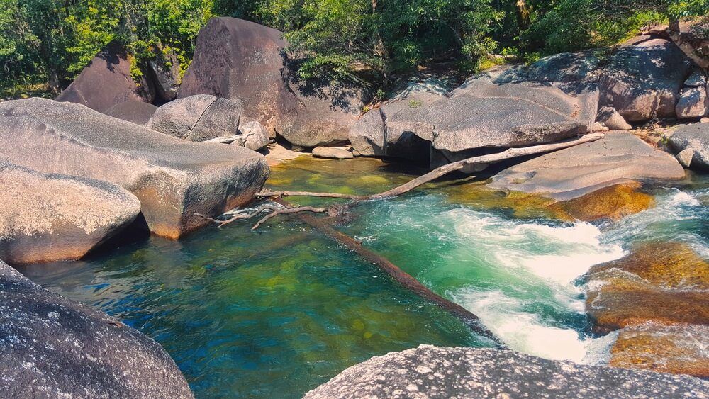 Fast-flowing turquoise water in a river surrounded by large gray rocks and a forest.
