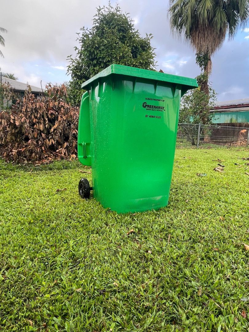 Green trash can on a grassy lawn, with trees in the background.— Greenaway Green Waste Removal in Mission Beach, QLD