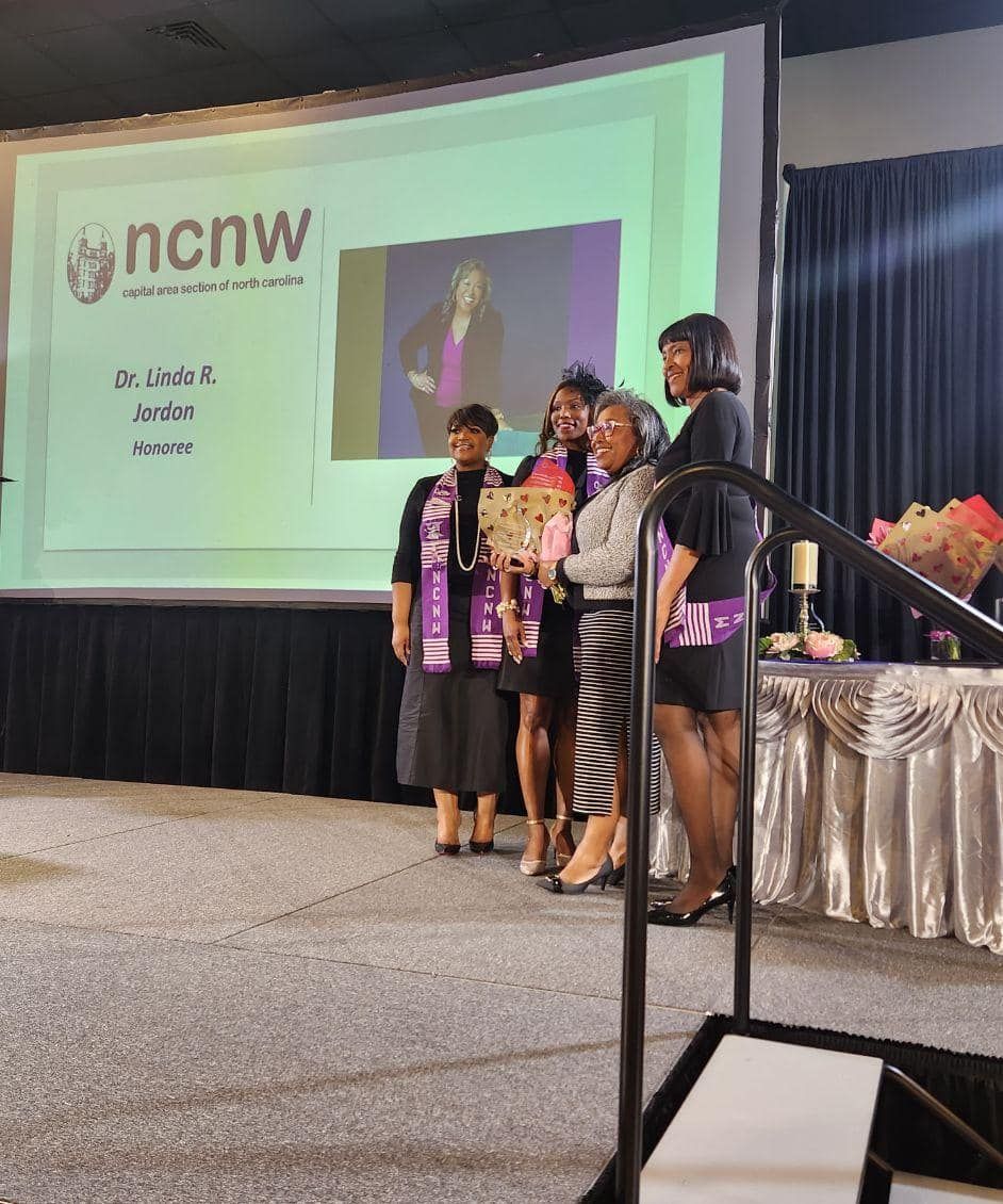 Group of women on stage, holding an award, in front of a screen with