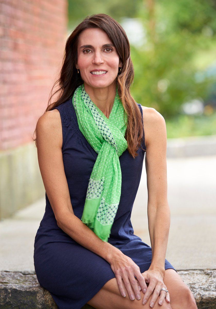 Woman in navy dress and green scarf poses outdoors.