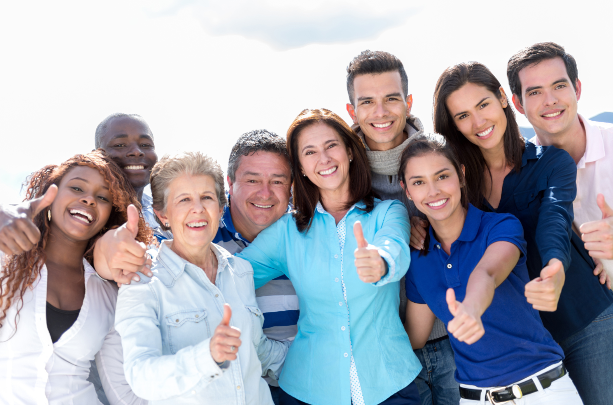 Diverse group of people smiling, giving thumbs up outdoors.